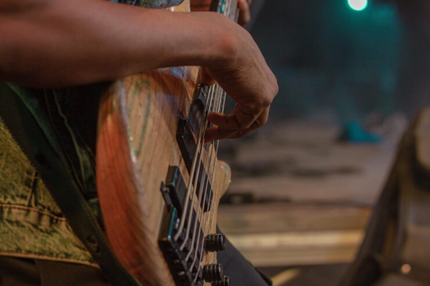 Close-up view of a person playing an electric guitar on stage, focusing on fingers strumming the strings under soft stage lighting.